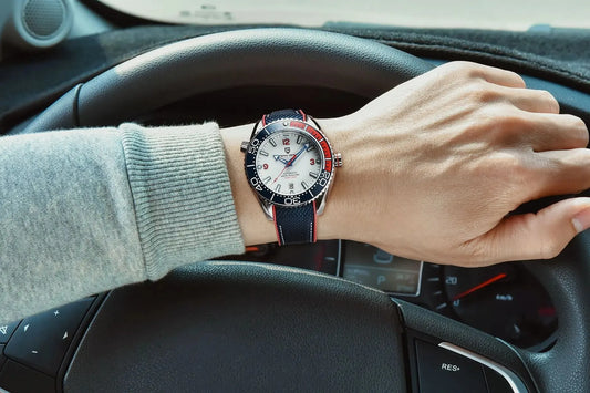 Relógio automático no pulso: mostrador branco e pulseira de tecido azul com detalhes vermelhos