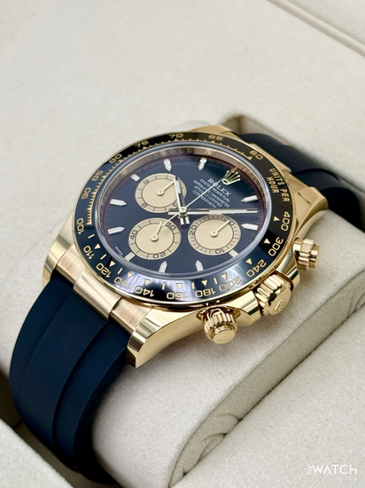 Relógio Daytona com caixa dourada, pulseira de borracha azul e mostrador escuro com cronógrafo.