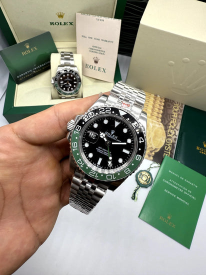Relógio Rolex GMT Master II na mão, mostrador preto, aro verde e pulseira de aço