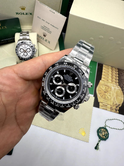 Relógio automático com mostrador preto e cronógrafo, pulseira de aço prateado ao lado