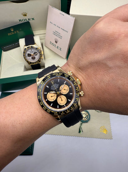 Relógio Daytona no pulso, caixa dourada e pulseira de borracha azul com cronógrafo.