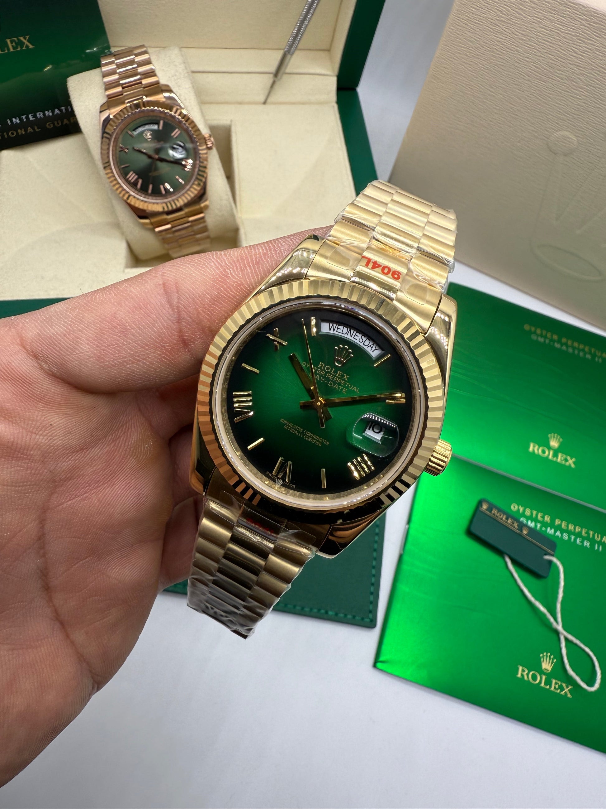 Relógio Rolex dourado verde com pulseira de metal e coroa lateral, na mão.
