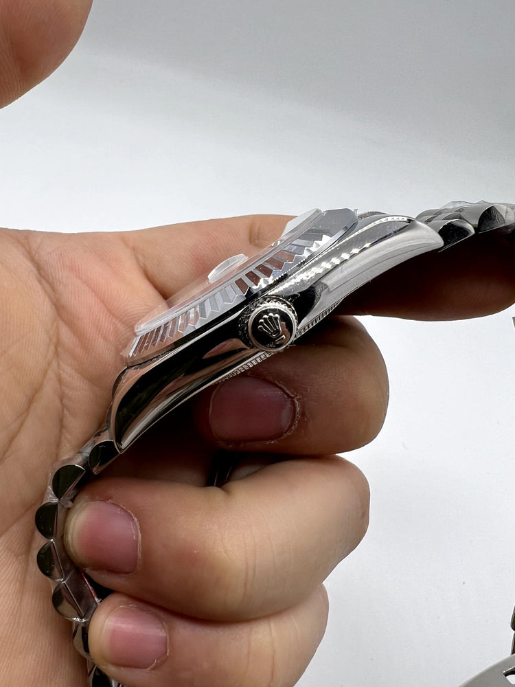 Relógio Rolex prateado de lado, com coroa e pulseira metálica, visto de perfil.