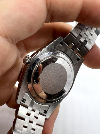 Relógio automático prateado com fundo e pulseira metálica em close, segurado na mão.