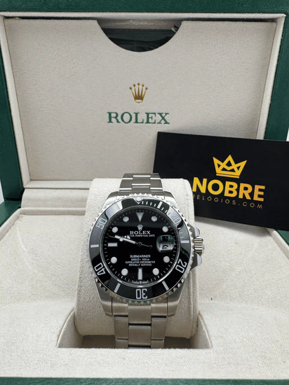 Relógio Rolex com mostrador preto e pulseira de aço, apoiado em estojo branco