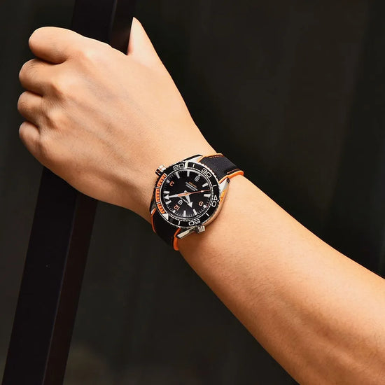 Relógio automático no pulso, mostrador preto com detalhes laranja e pulseira laranja