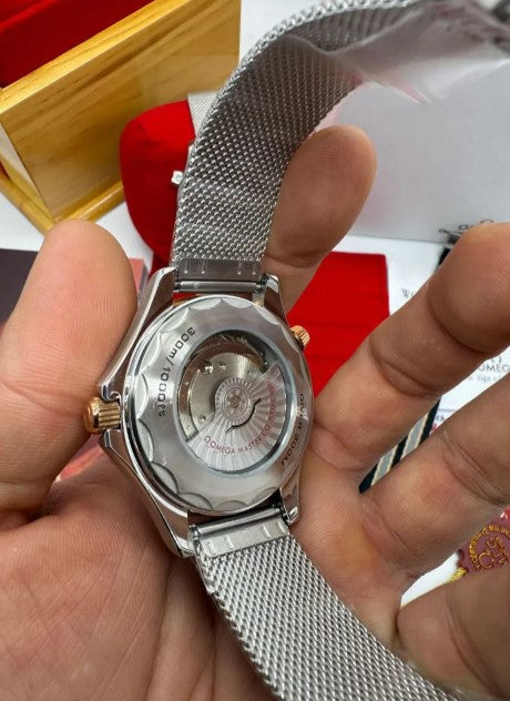 Relógio Omega com tampa traseira aberta na mão, pulseira mesh prateada