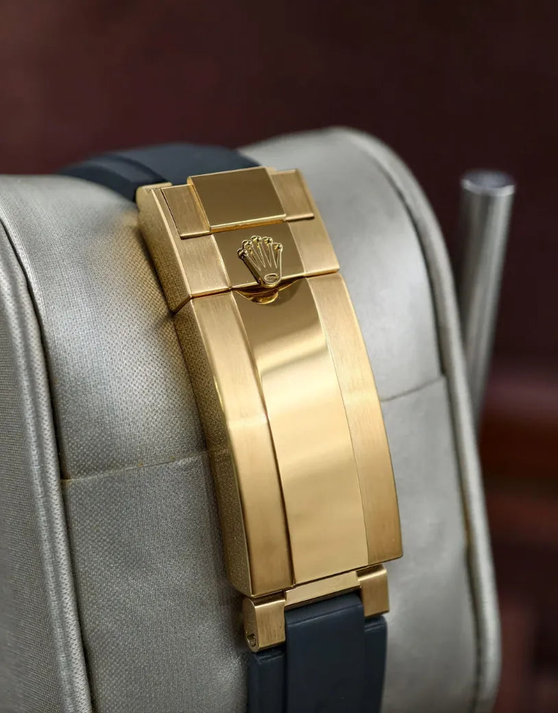 Pulseira do relógio Rolex com fecho dourado retangular, sobre base clara.