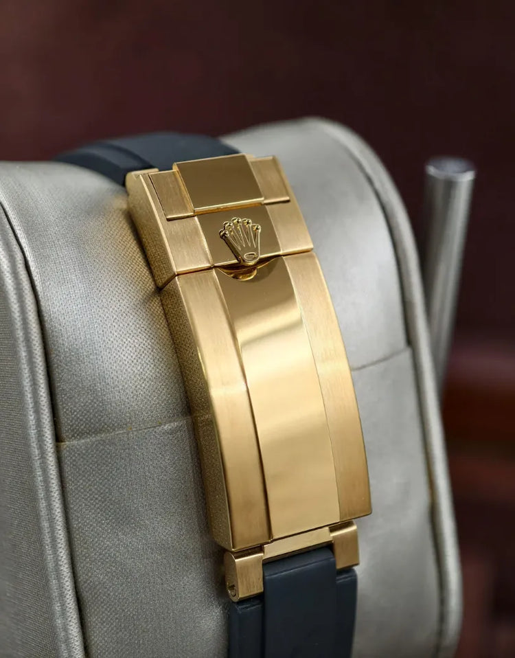 Pulseira do relógio Rolex com fecho dourado retangular, sobre base clara.