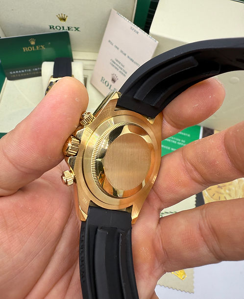 Relógio Daytona com caixa dourada e coroa, pulseira de borracha azul na mão.