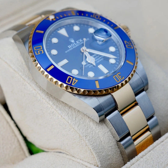 Relógio Rolex Submariner com luneta azul e pulseira bicolor aço e dourado, close.
